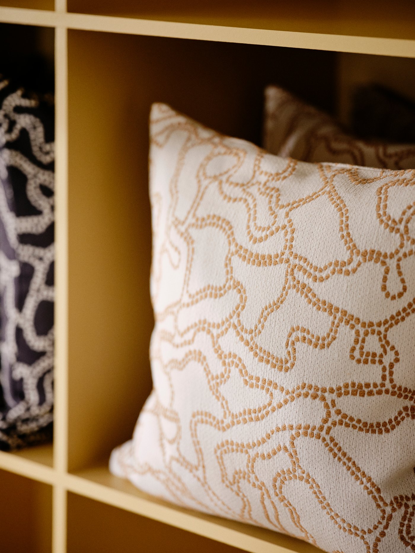 An off-white GULDFLY cushion cover with jacquard-woven pattern in yellow-beige, stored in a shelving unit.
