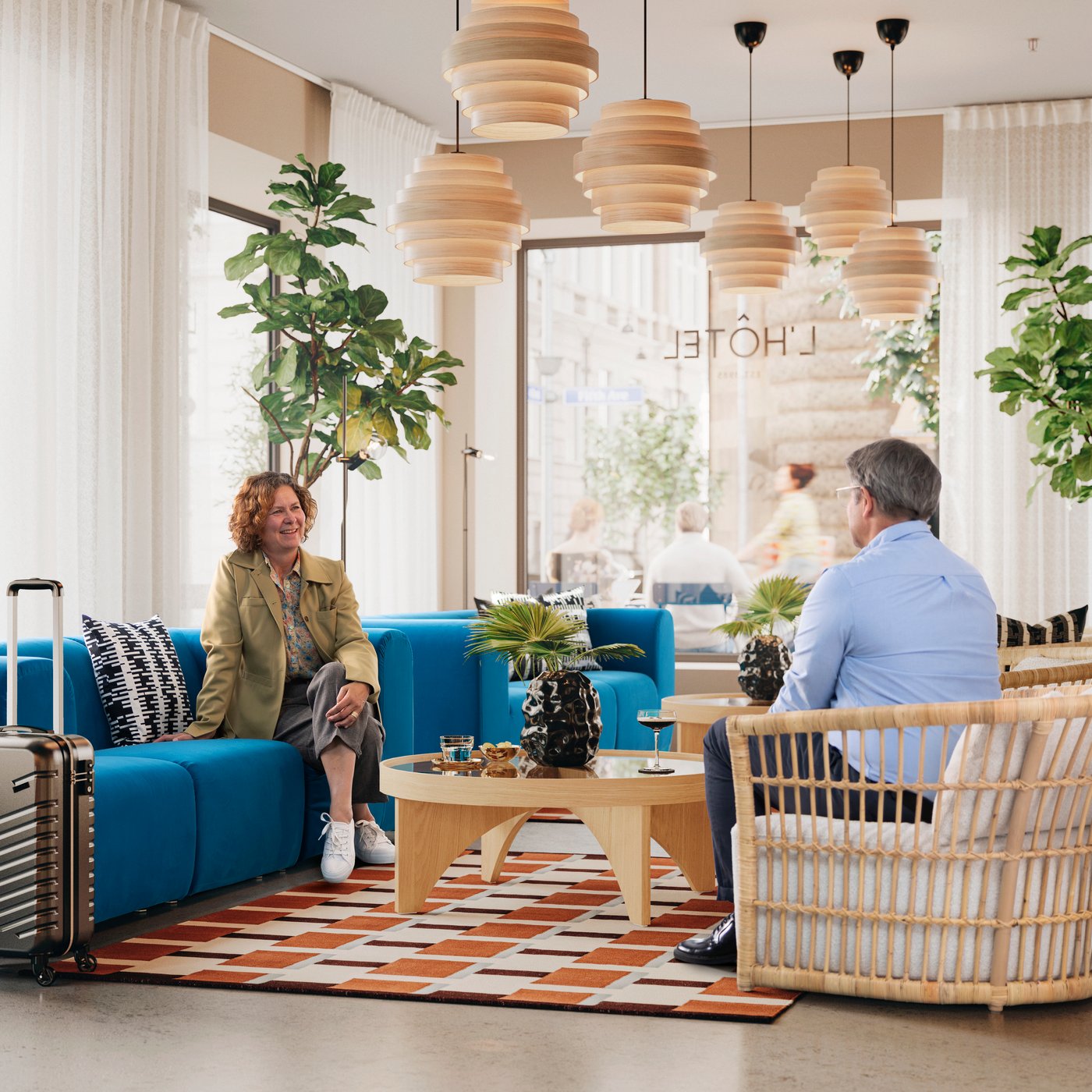 Hotel lobby scene with a grey/white STOCKHOLM 2025 rattan armchair, a sofa, coffee table, and two people sitting and talking.