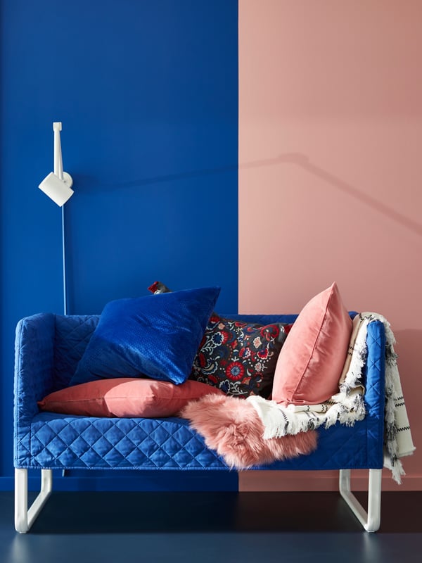 A turquoise sofa with brown and beige cushions, a beige rug, beige and orange curtains, a large round mirror.