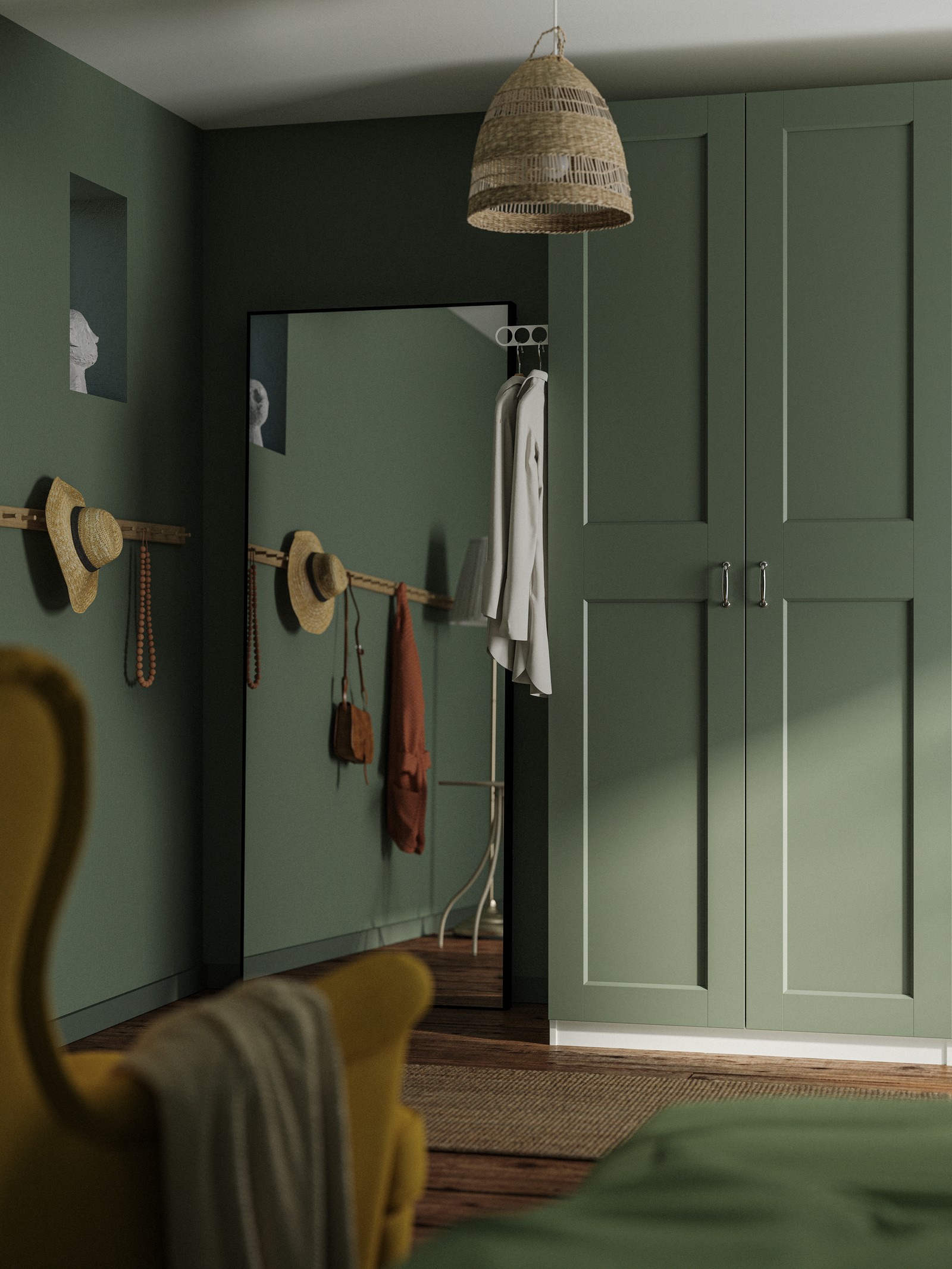 Ugao spavaće sobe sa zelenim zidovima, ogledalom, PAX/GRIMO sivo-zelenim garderoberom i delimično vidljivom žutom STRANDMON foteljom.