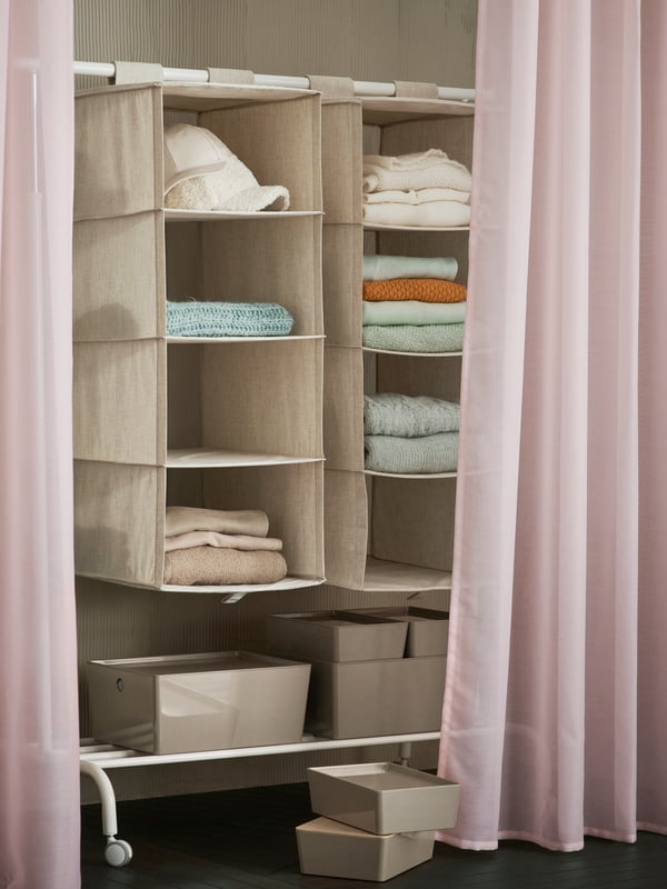 A white RIGGA clothes rack with a PURRPINGLA organiser in the storage room, along with a pair of pink STENFRÖ sheer curtains.