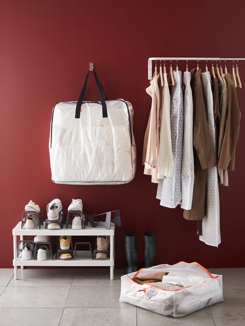 PÄRKLA storage case on tile floor next to shoe stand, a rail of clothes on hangers and a DIMPA storage bag on wall hook.