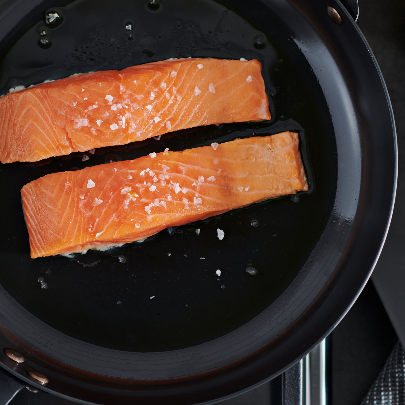 Two SJÖRAPPORT salmon fillets in a VARDAGEN carbon-steel frying pan placed on a gas hob.
