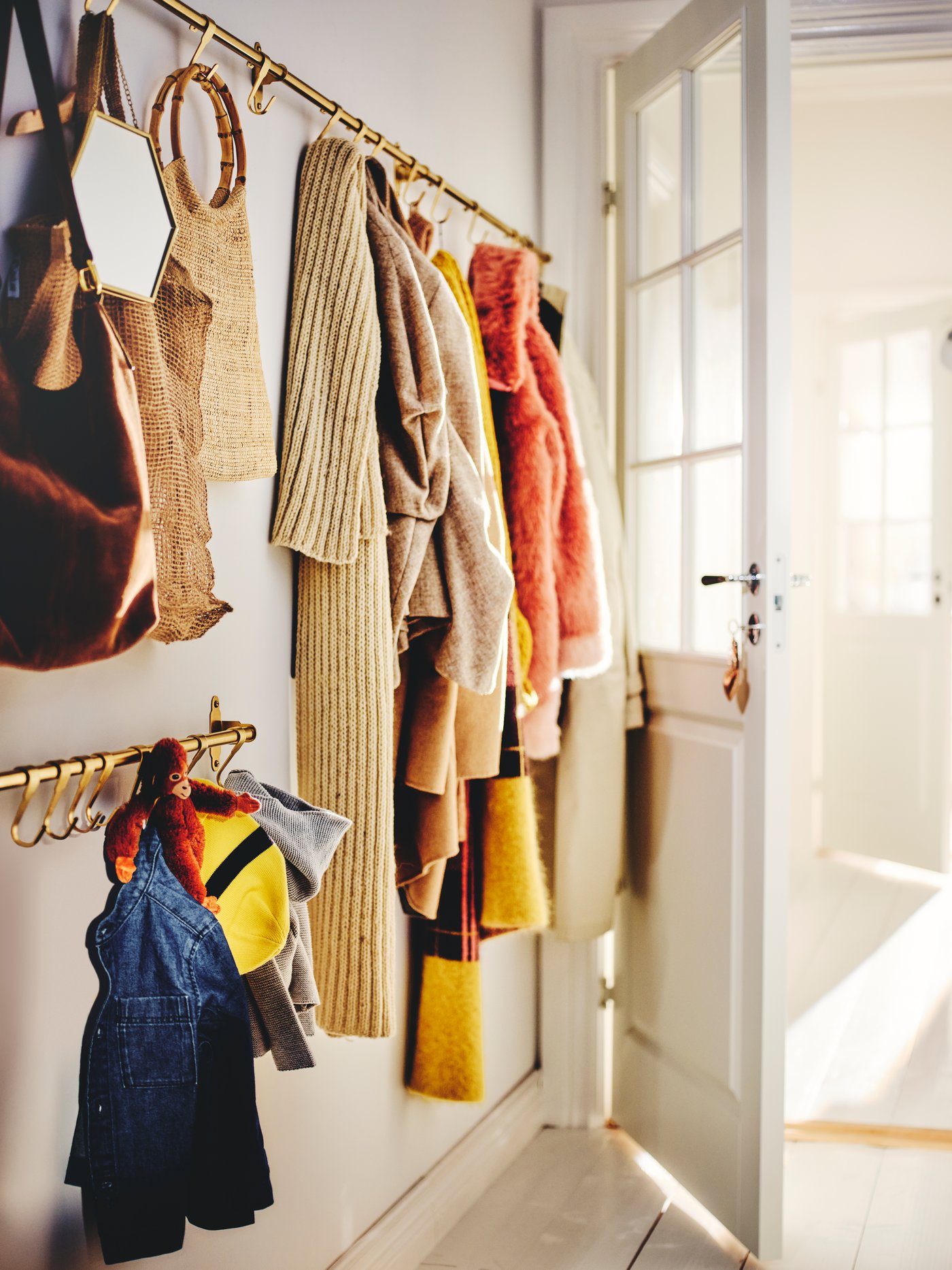 Clothes, bags, a mirror and a toy hanging from HULTARP hooks, set on brass-coloured HULTARP rails in a hallway.