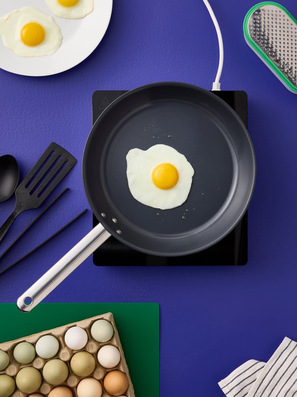 An IKEA 365+ frying pan in stainless steel with non-stick coating on a TILLREDA portable induction hob has a fried egg in it.