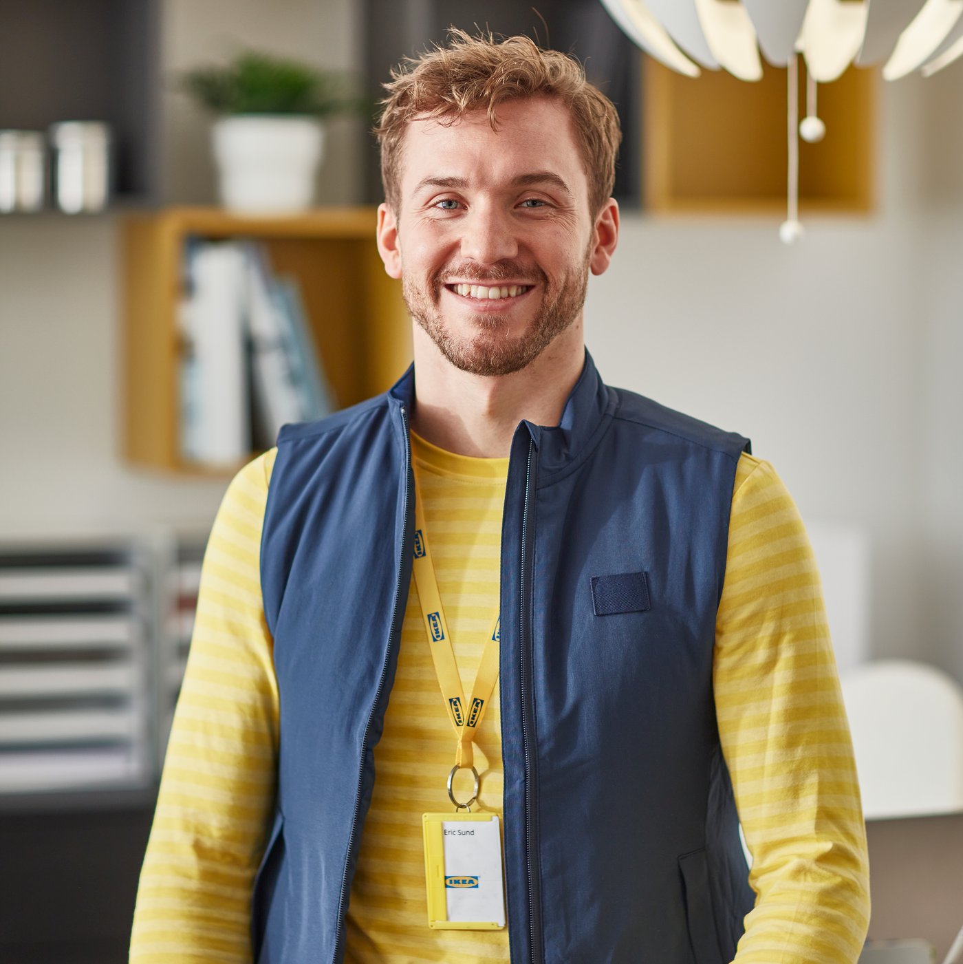 An IKEA employee working on a laptop, chatting with customers.