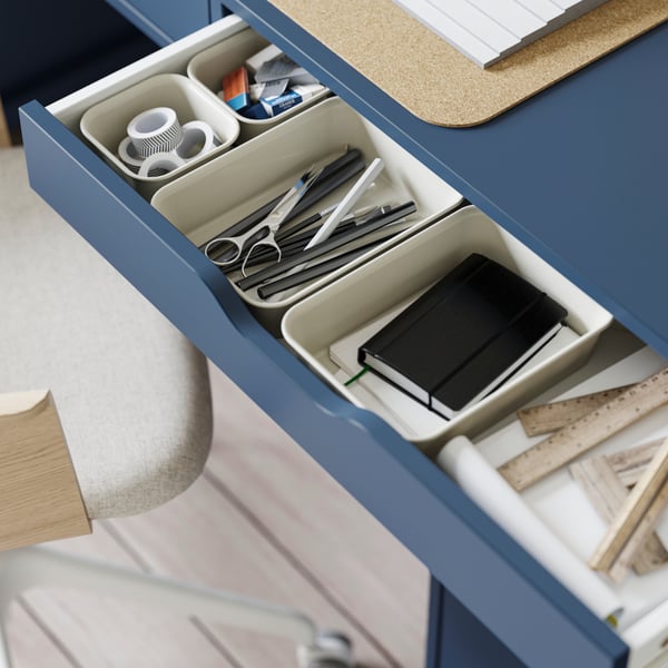 An opened drawer of the ALEX desk in black-blue, filled with study supplies divided in beige NOJIG organisers.
