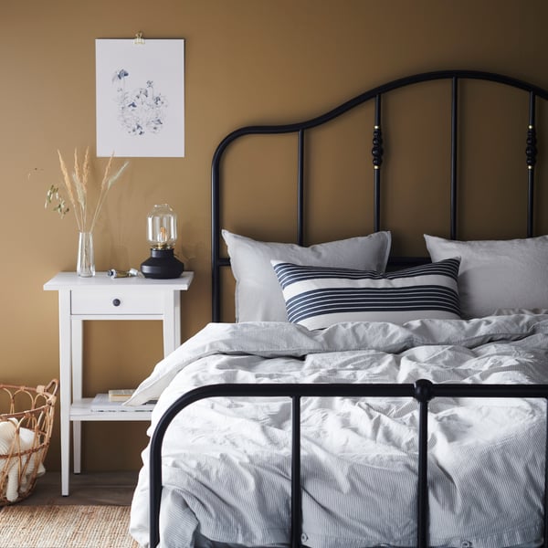 Une chambre à coucher avec des murs beiges, un grand lit et une table de chevet blanche.