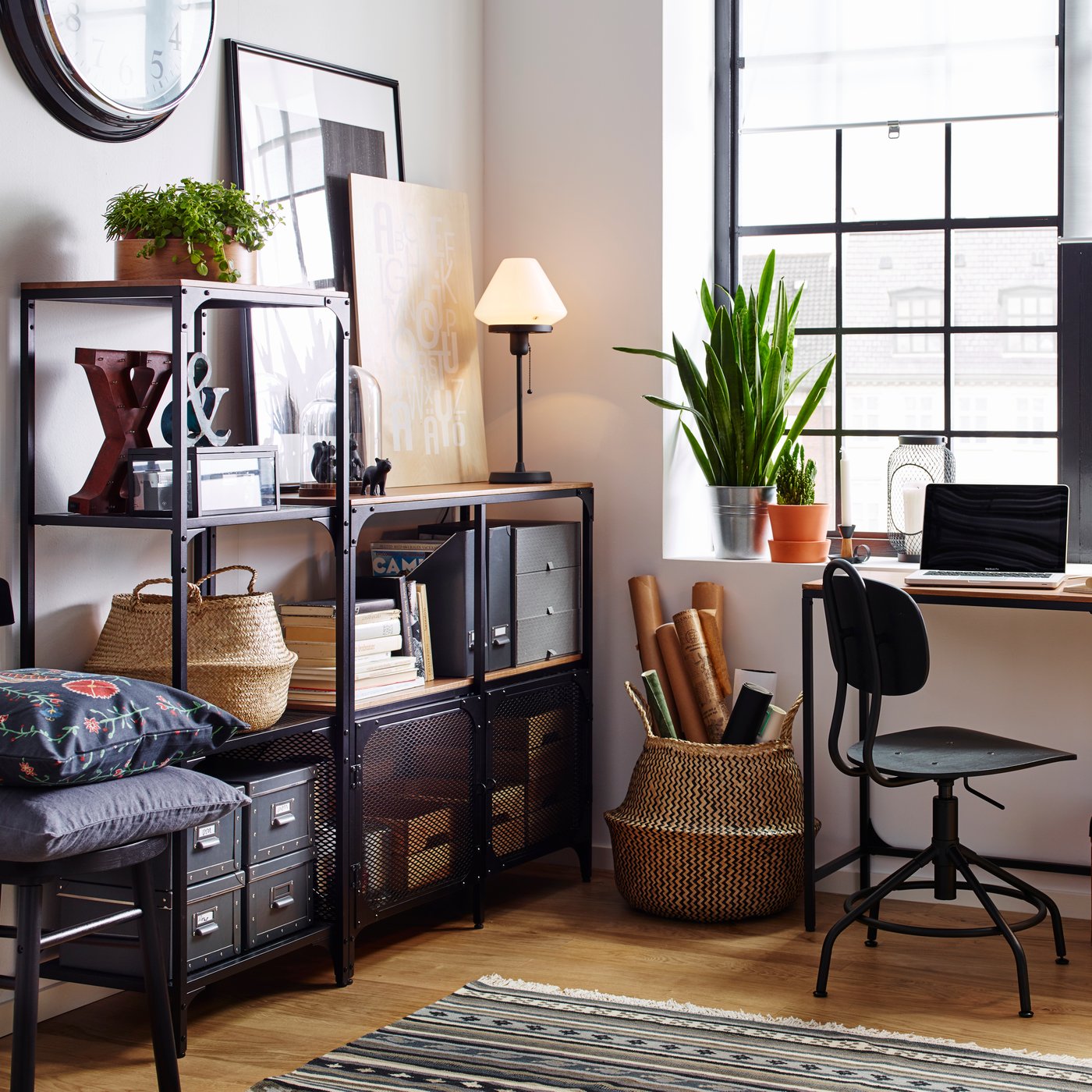An industrial-style living room with a black metal open shelving unit featuring paintings, a table lamp, and a black office chair.