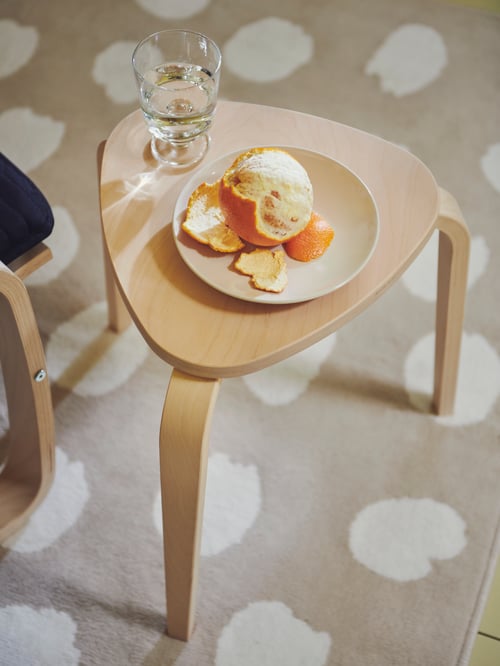 Overhead shot of a beige stool with a partially peeled orange on a side plate, and a goblet. The stool is on a rug.