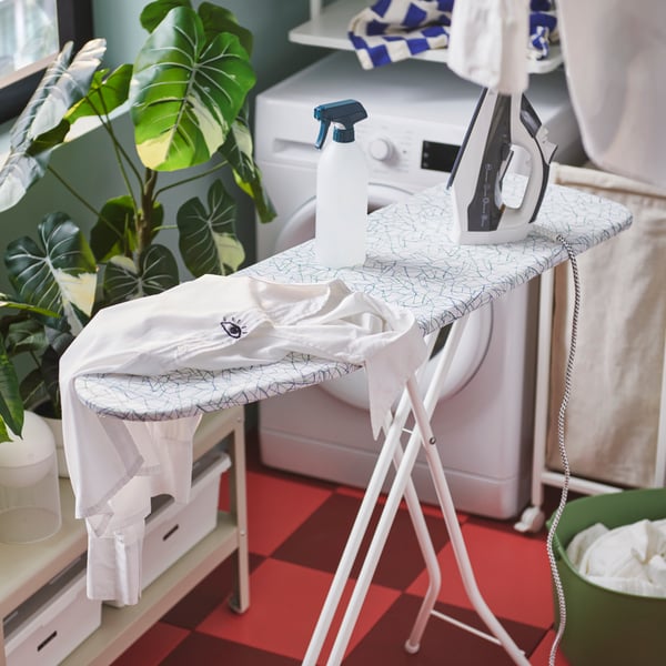 A white RUTER ironing board with a patterned cover holds a shirt and iron, in a light-filled, enclosed balcony laundry area.