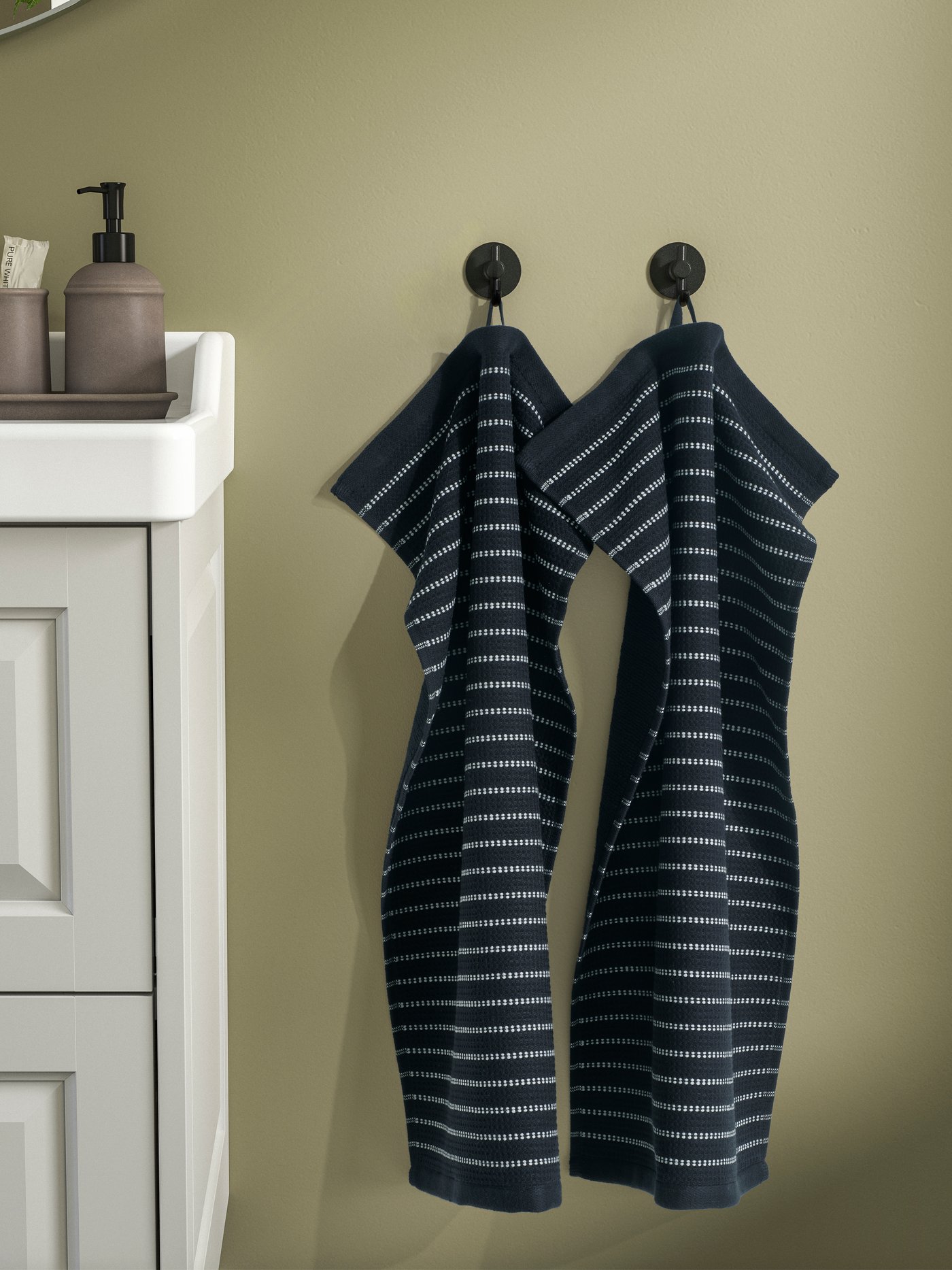 白い洗面台とキャビネット、ソープディスペンサー、歯ブラシホルダー、ベージュの壁に掛けられた紺色のストライプ柄タオル2枚があるバスルームの様子。