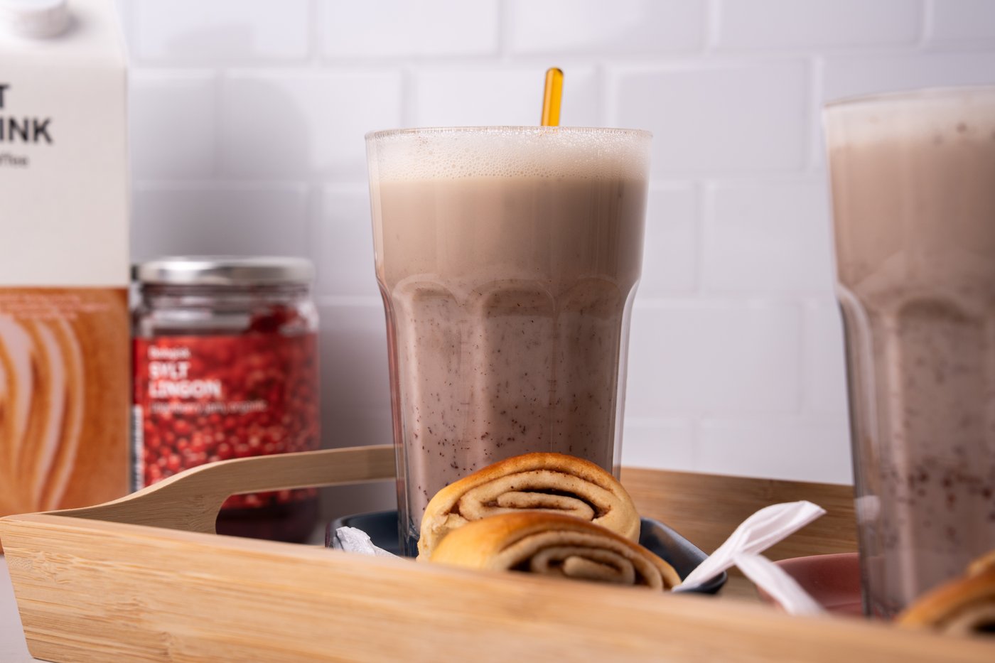 Ein Haferlatte in einem Glas, welches mit Zimtschnecken auf einem Holztablett präsentiert wird.
