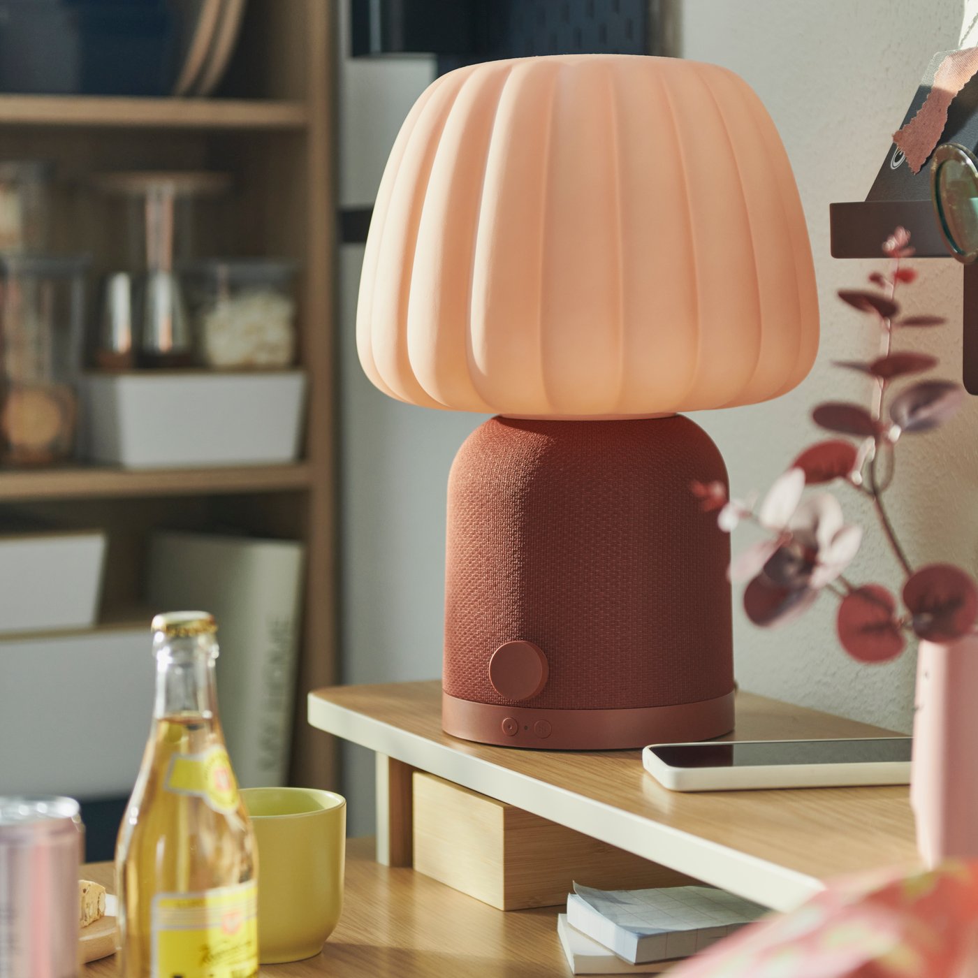 A dorm room features a brown and pink KULGLASS Bluetooth speaker lamp on a wooden table, with a softdrink in the foreground.