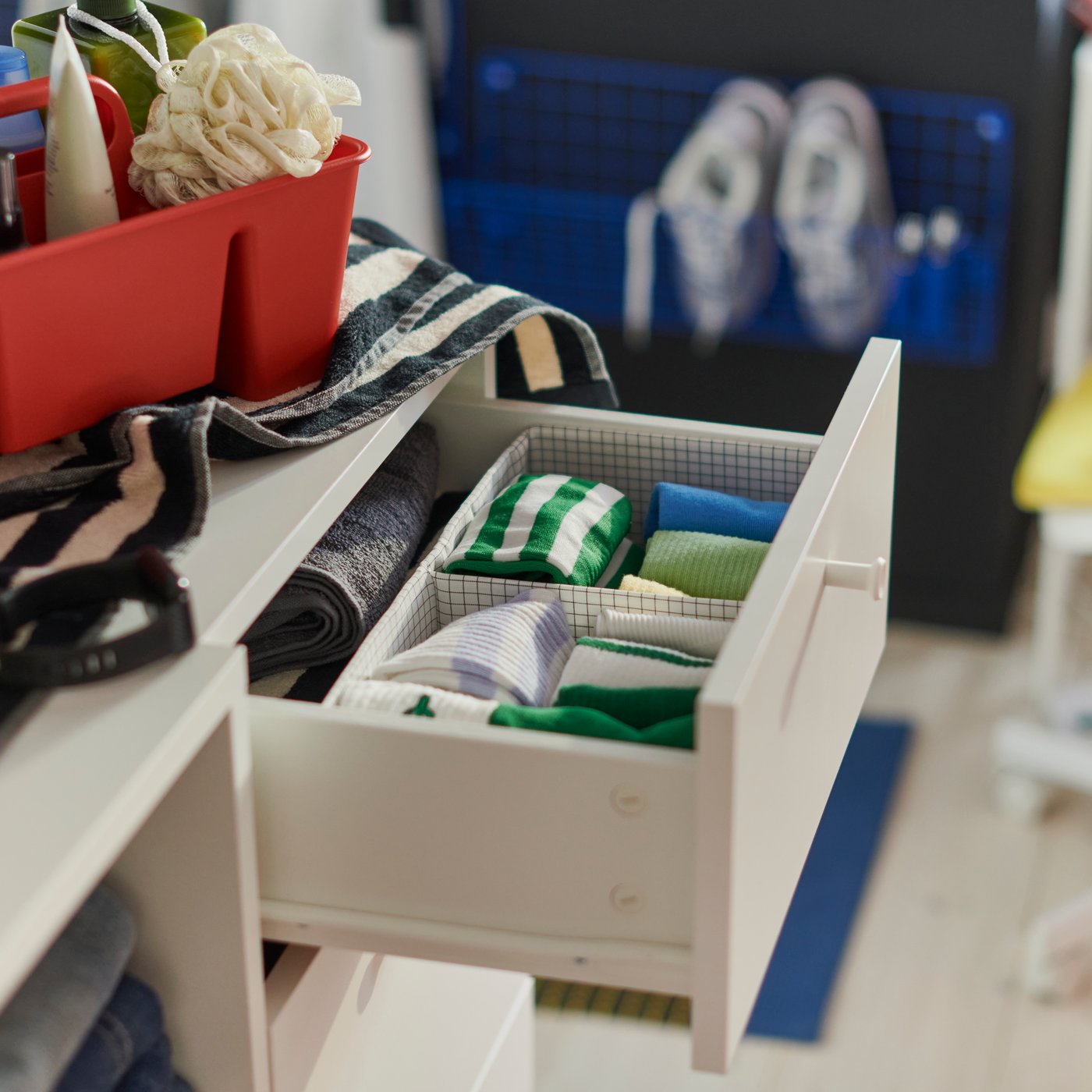 A close-up of a white LASTARE combination with drawers open, showing neatly folded clothes and a red storage box on top.