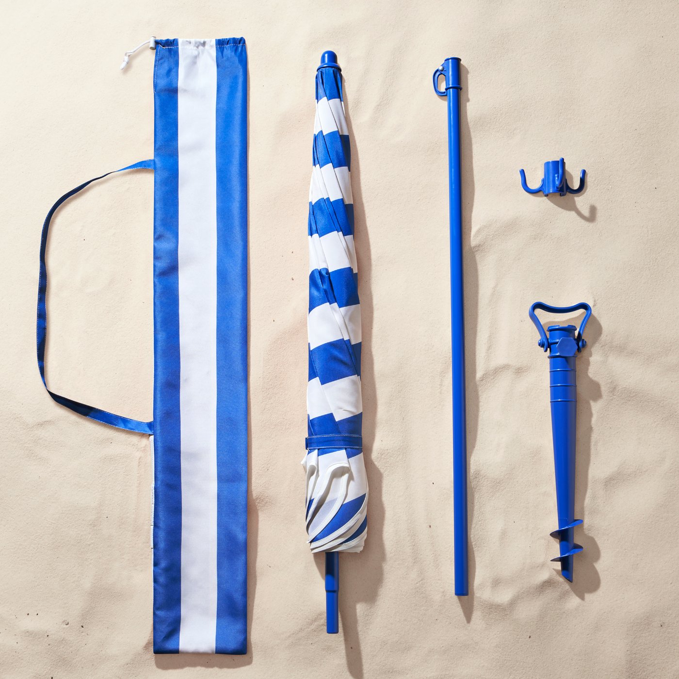 Bovenaanzicht van de onderdelen van een STRANDÖN parasol en de draagtas die in het zand liggen.