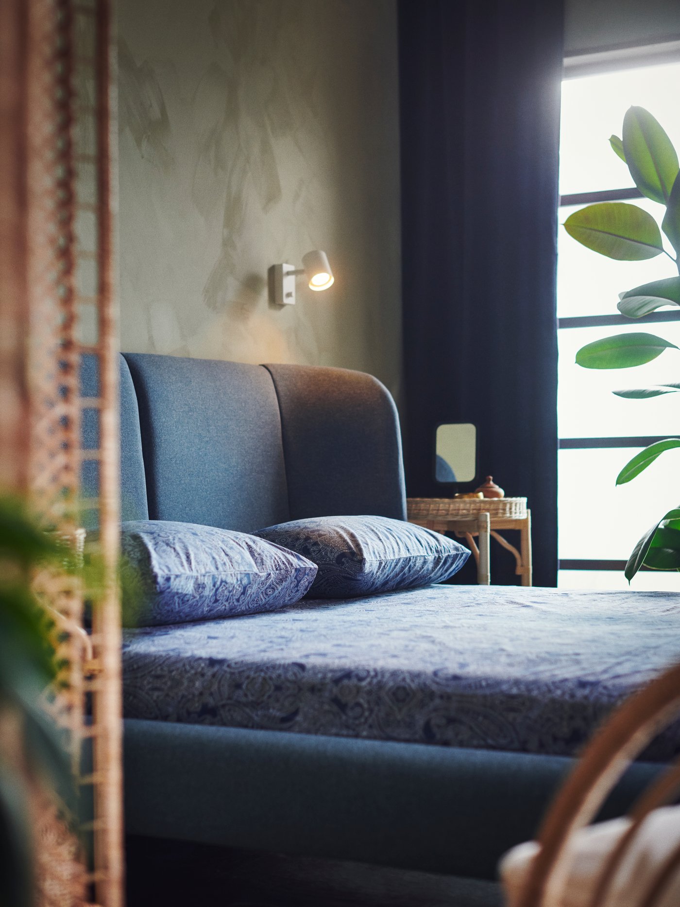 A blue TUFJORD upholstered bed is covered with JÄTTEVALLMO bed linen. A NYMÅNE light is mounted to the wall.