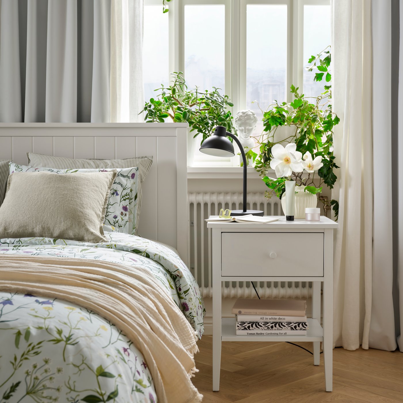 A bedroom with a white GULLABERG bedside table featuring a drawer and shelf beside a GULLABERG bed frame with floral bedding.