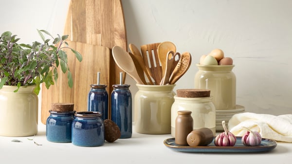 Beige and blue glazed stoneware jars with cork lid on kitchen countertop used to store olive oil, utensils, herbs and eggs.