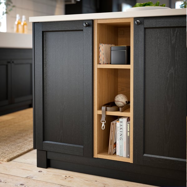 A kitchen with black LERHYTTAN fronts and a wooden open cabinet for recipe books and accessories.