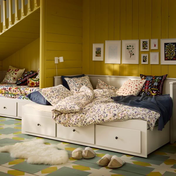 Ein augeklapptes weißes HEMNES Tagesbett mit bunter Bettwäsche.