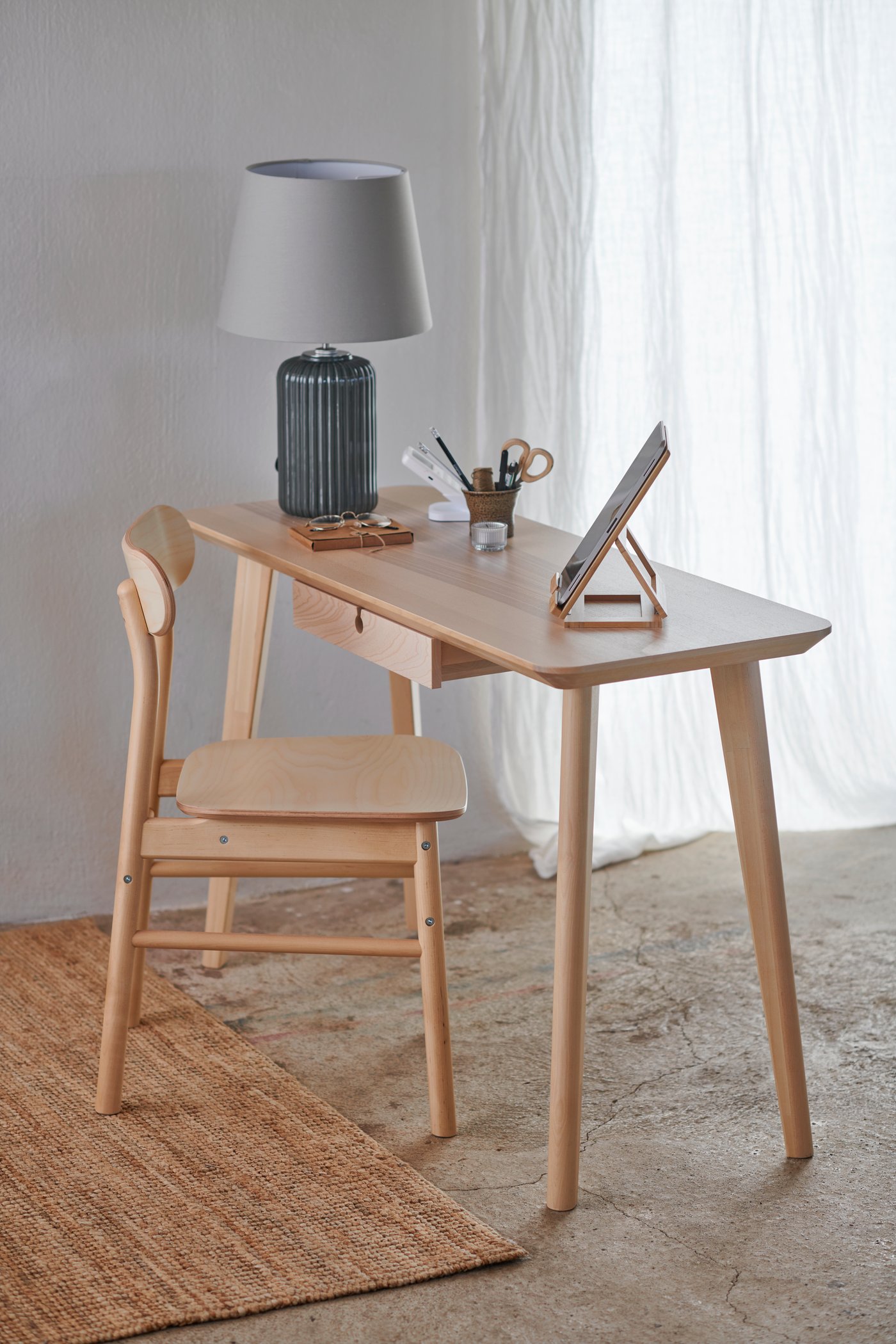Una scrivania LOHALS in legno con una lampada da tavolo e un porta tablet e una sedia in legno.