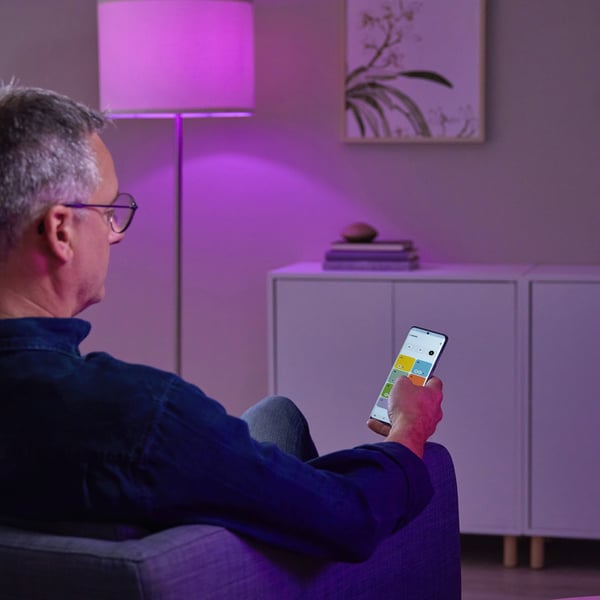 En mand sidder i en stol med en mobilenhed i hånden og ser på IKEA Home smart app aktiveret af DIRIGERA hub.