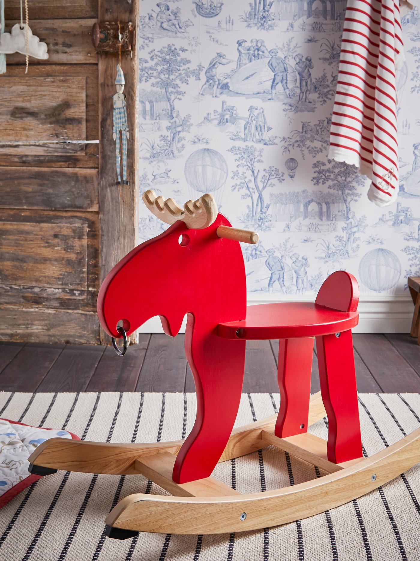 An EKORRE rocking-moose stands on a TÖRSLEV flatwoven rug in a children’s room with blue and white wallpaper.