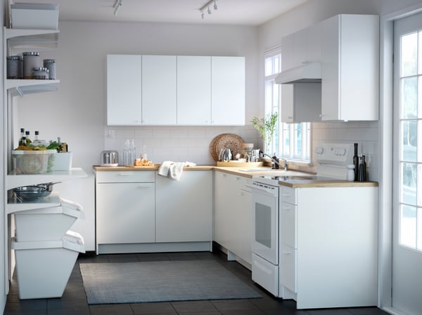 Una cucina KNOXHULT bianca angolare. A lato, alcune mensole con barattoli e contenitori. Accanto alla cucina c'è una porta finestra che illumina la stanza.