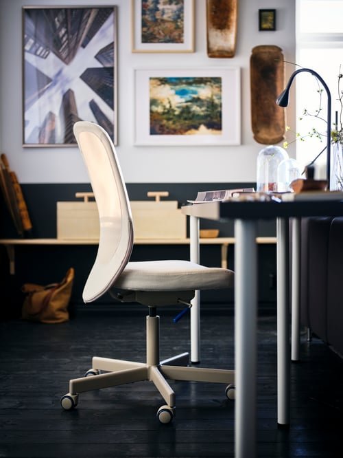 Focalizarea spațiului de lucru al unui scaun de birou bej cu rezistență reglabilă lângă o tăblie dreptunghiulară a mesei cu picioare albe.