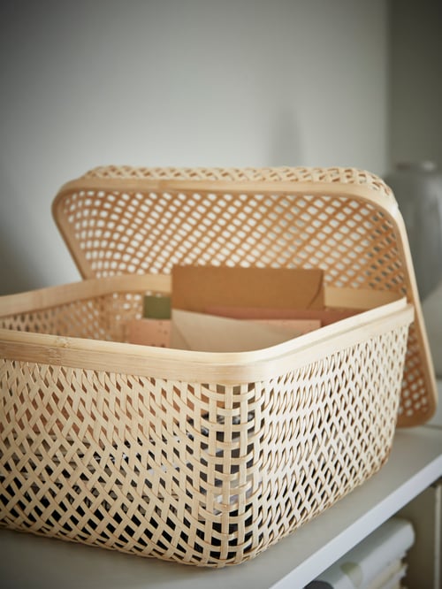 Un prim-plan al unei cutii dreptunghiulare cu capac cu un design țesut. Capacul se sprijină pe una dintre părțile laterale ale cutiei.