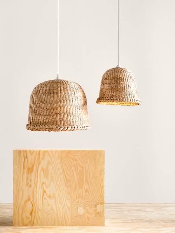 Two MÄVINN pendant lampshades in different sizes are hanging next to each other over a plywood pedestal against a white wall