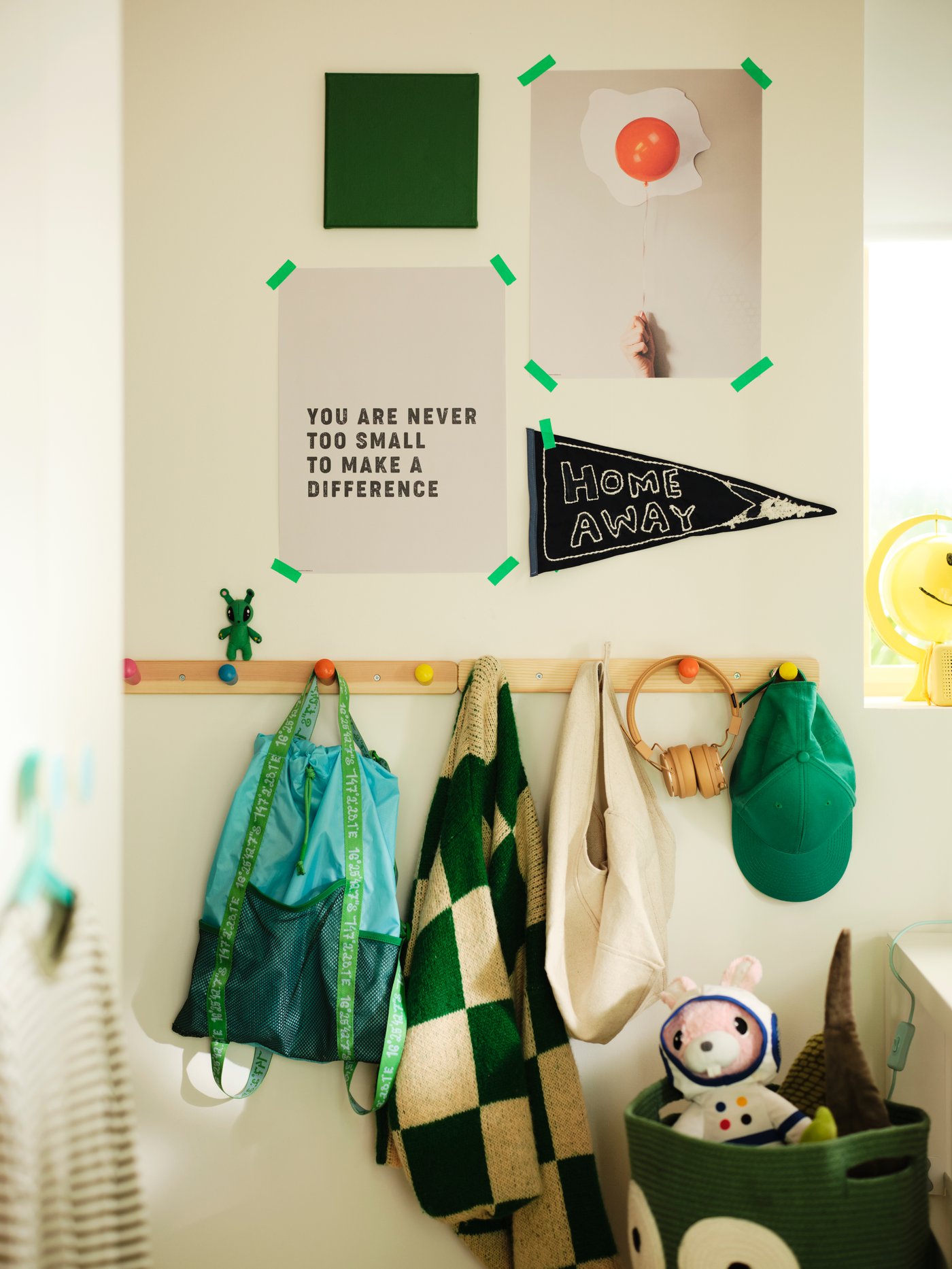 A wall shows tacked up posters with FLISAT hooks underneath. Bags, headphones and clothes hang from the hooks.