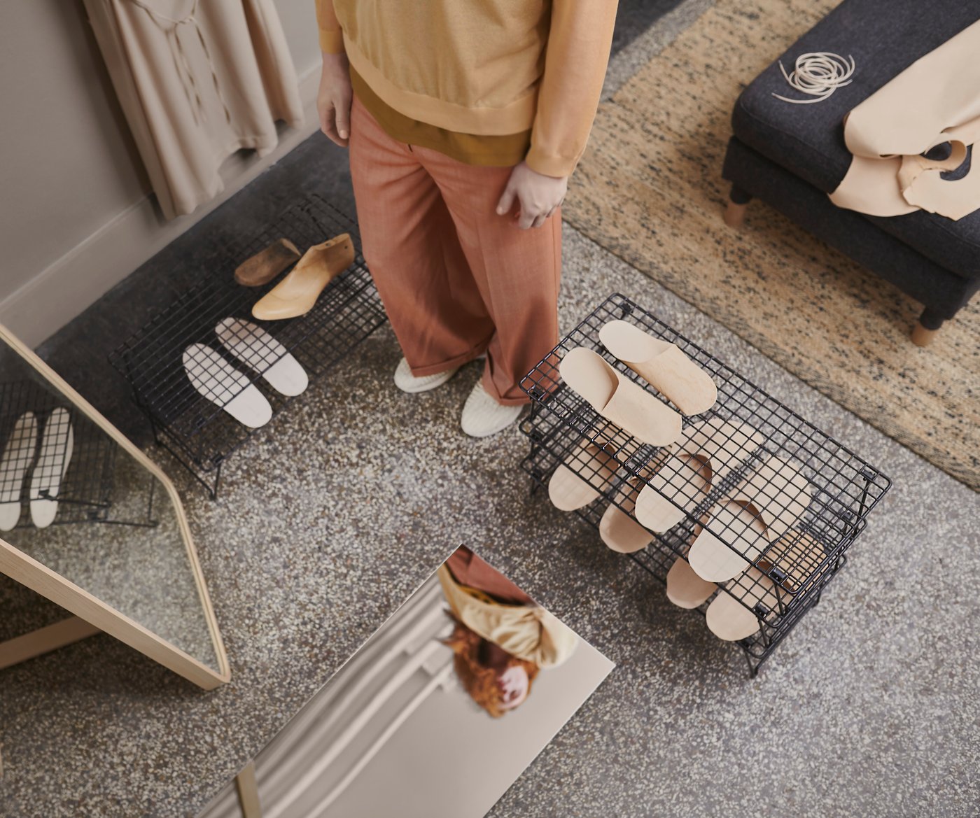 A hallway with two black GREJIG shoe racks holding slippers, a person standing between them, plus two mirrors on the floor.
