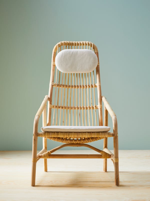 Avant d’un fauteuil en rotin SALNÖ avec jeu de coussins GRYTTOM dans une pièce avec un sol en bois et des murs gris/vert.