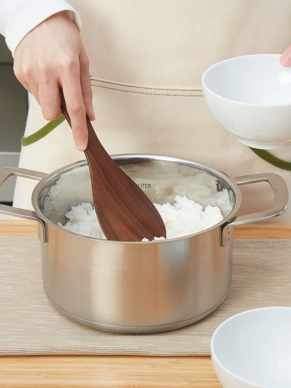 Olla HEMKOMST con una cuchara de madera HULDHET con arroz en su interior.