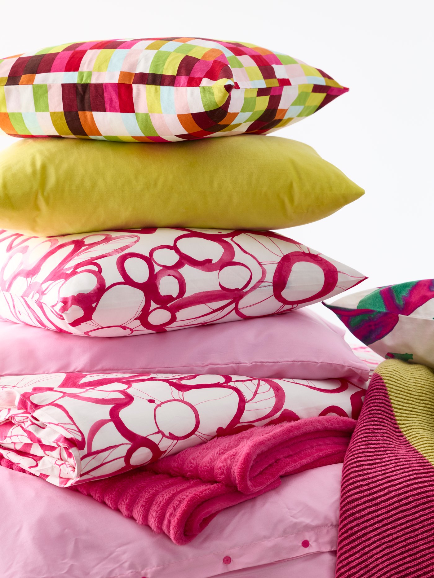 Showing new cushions such as HÄRLIR and LÖVNATURSKOG stacked on top of each other on a bed. 