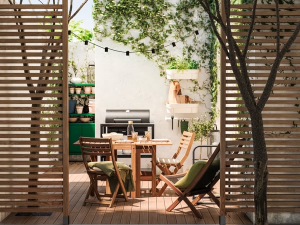 Das ist ein Bild von einem Garten mit einem Tisch und 2 STühlen im vordergrund. Daneben steht ein Griller.