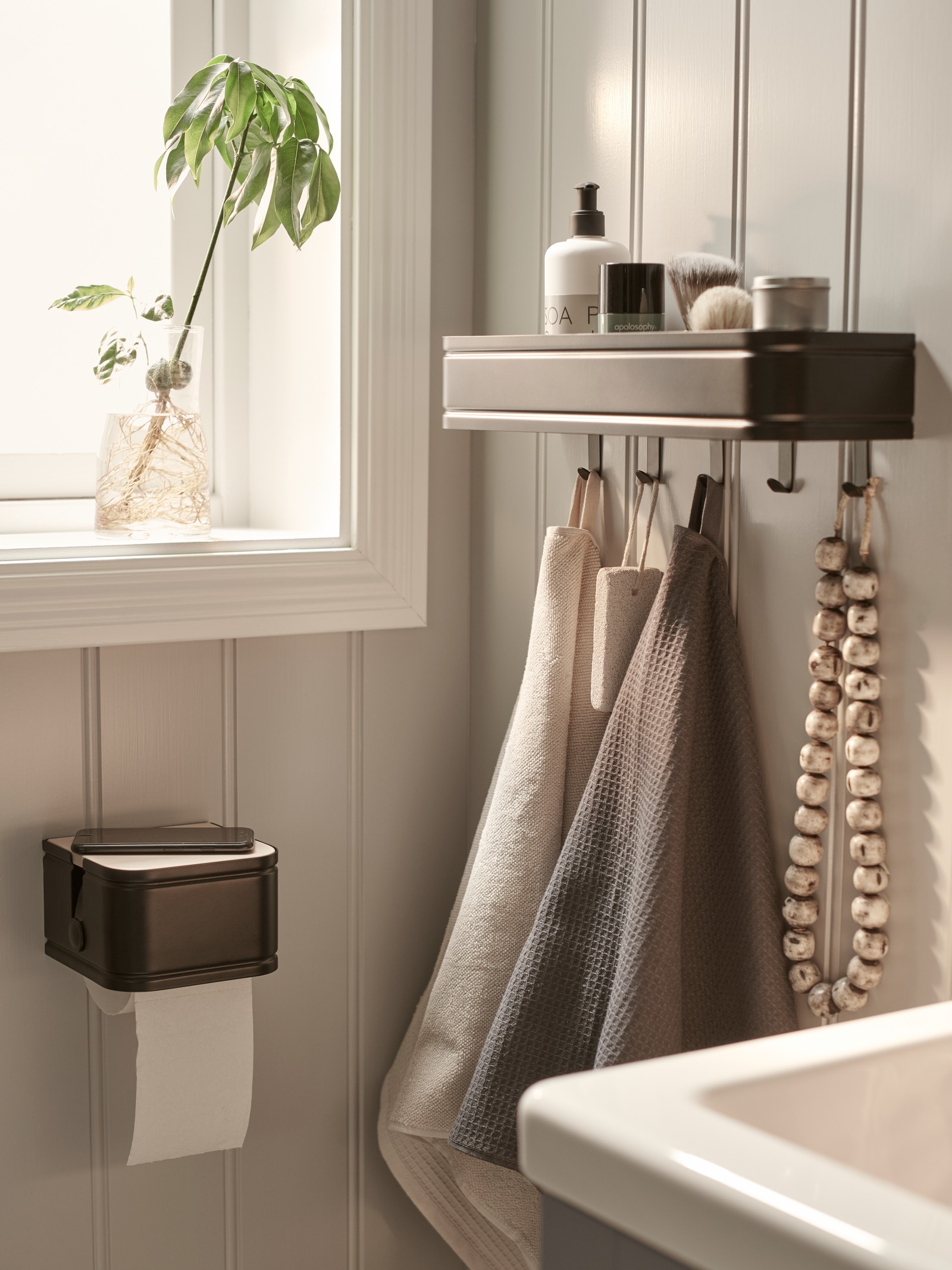 Un baño con una repisa LILLASJÖN negra con cremas y otros artículos en su interior.