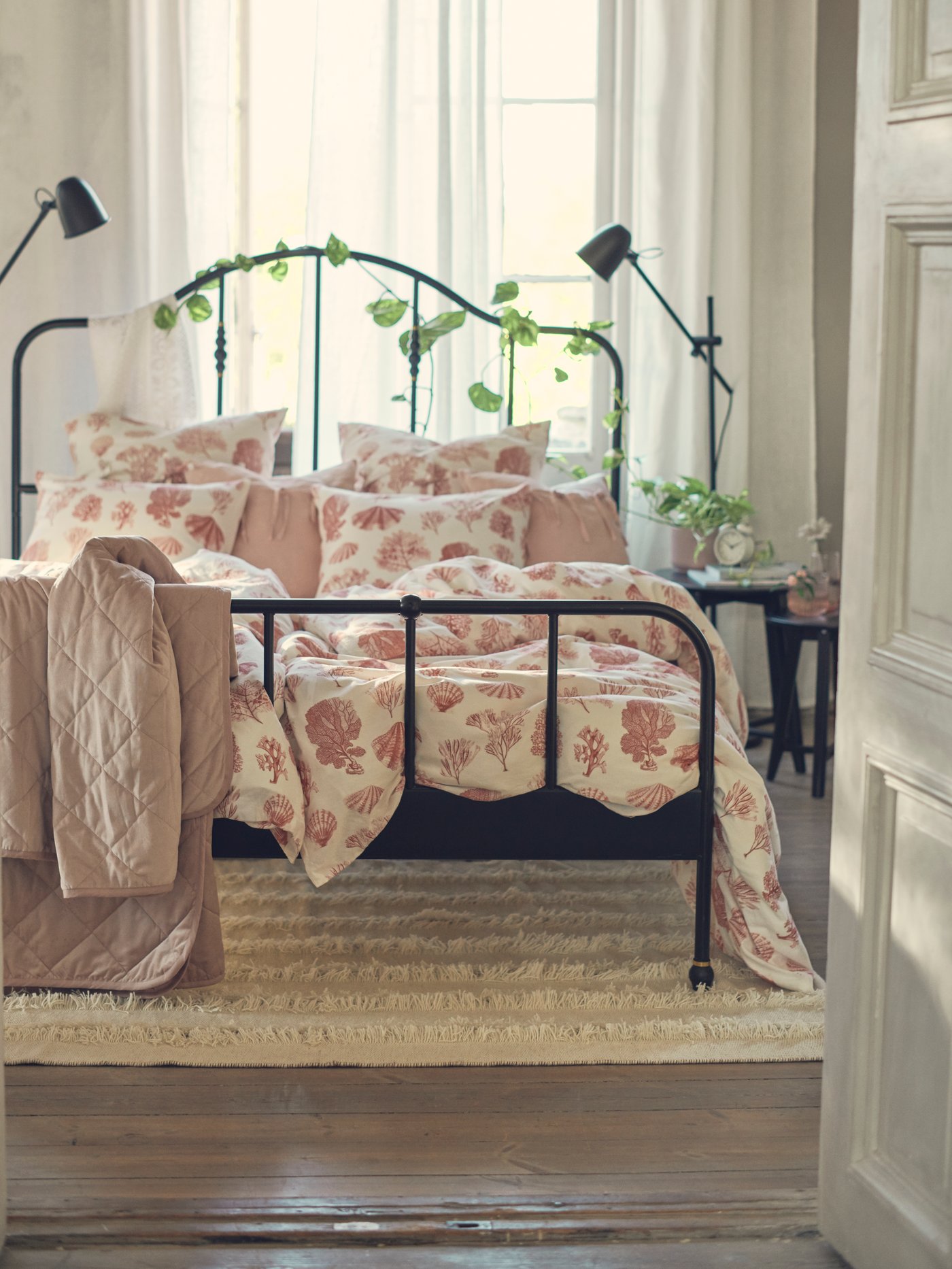 Una cama de fierro con ropa de cama rosada en una habitación matrimonial.