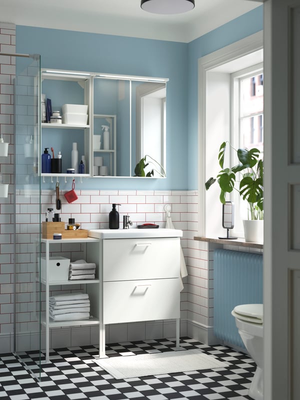 Un baño con muebles para ENHET blancos. El piso del baño tiene recuadros negros y blancos.