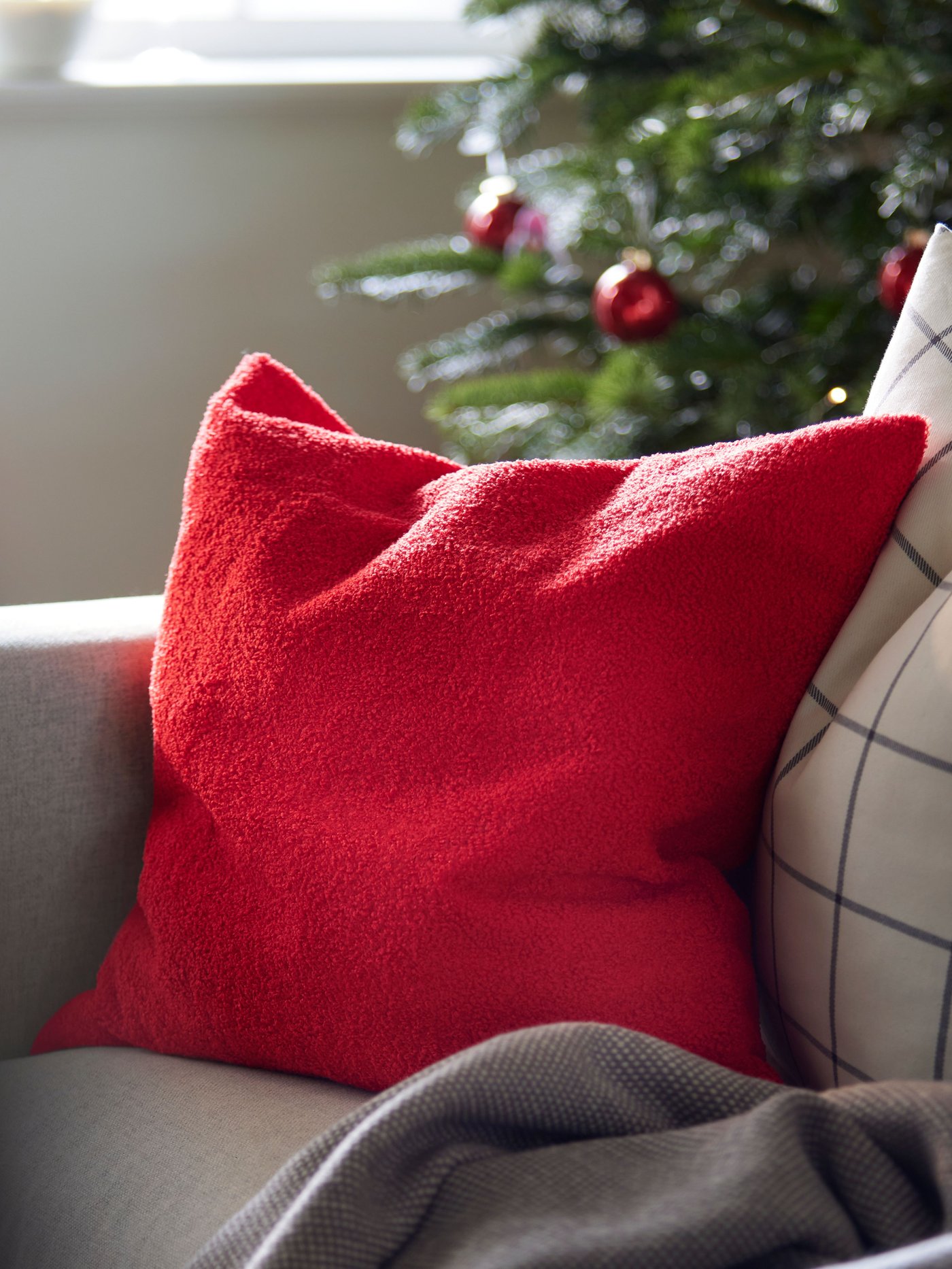 A GRÖNLID sofa with cushions in a red/brown SANELA cover and a SNÖBRACKA cover stands in front of a window.