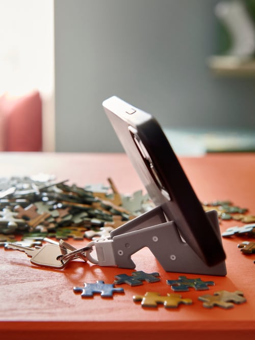 Un suport pentru telefonul mobil YUPPIENALLE pe o masă roșie, înconjurat de piese de puzzle multicolore.