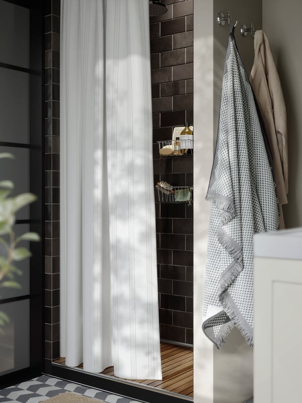 A spa bathroom showing part of a shower with white patterned shower curtain and a FJÄLLSTARR bohemian cotton towel on a hook.