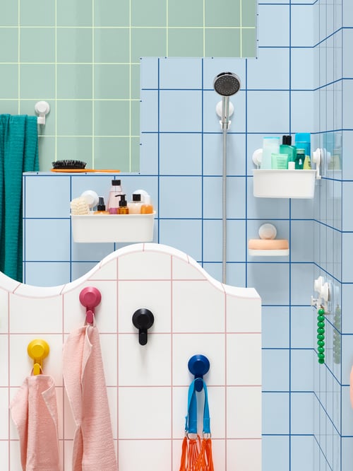 A display of different-coloured, tiled walls, with suction cup bathroom accessories like hooks and a white TISKEN basket.