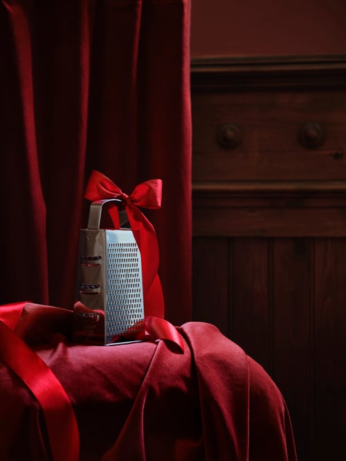 Close-up of kitchen corner with red curtains, stainless steel grater with a red ribbon on the handle, red household textile.