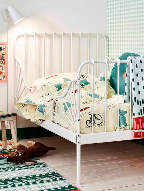 A MINNEN extendable bed with KÄPPHÄST bed linen in the corner of a bedroom near a FUBBLA LED wall lamp.