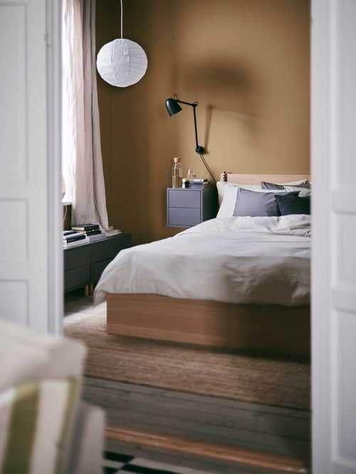 Bedroom that features a bed frame with two storage boxes, a cabinet with two drawers, and a carafe with stopper.
