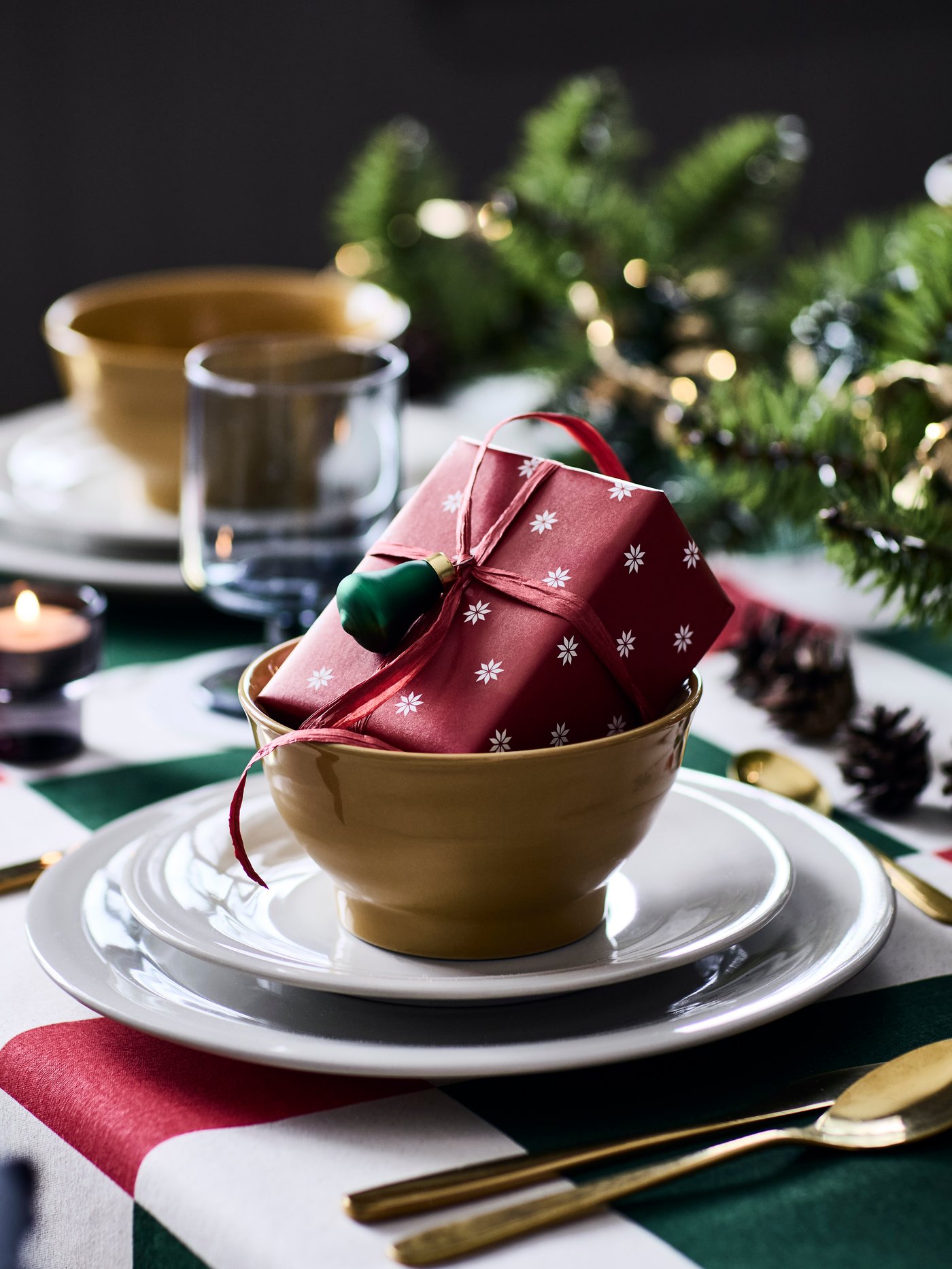 A small present sits in a bowl on a festive dinner table, wrapped in a red VINTERFINT gift wrapper with a snowflake pattern.