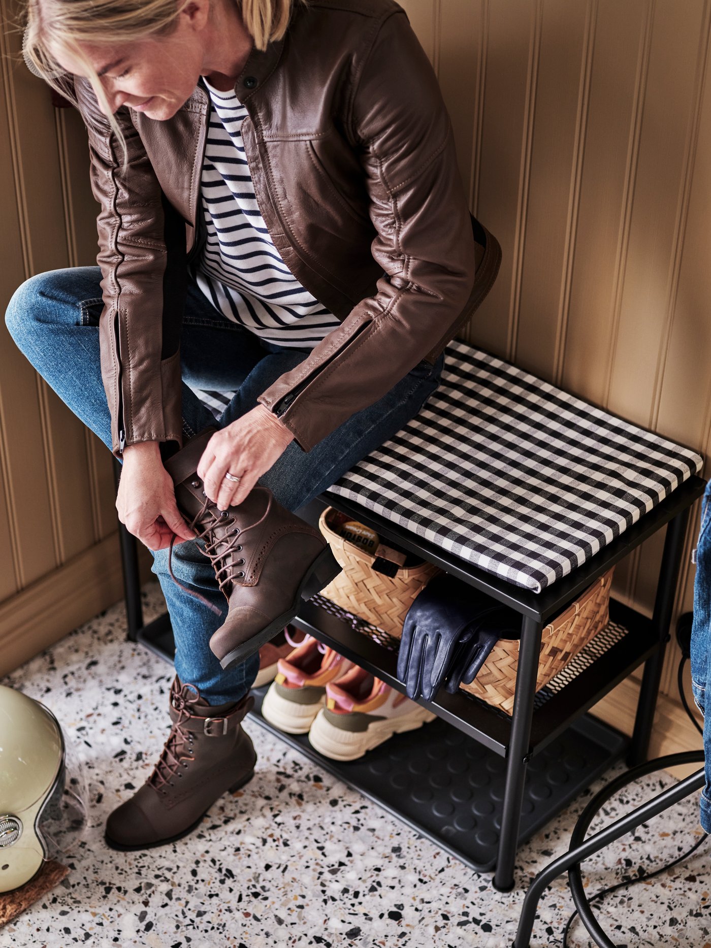 A person ties a bootlace while sitting on a NIPÅSEN bench with shoe storage with a black BAGGMUCK shoe tray underneath.